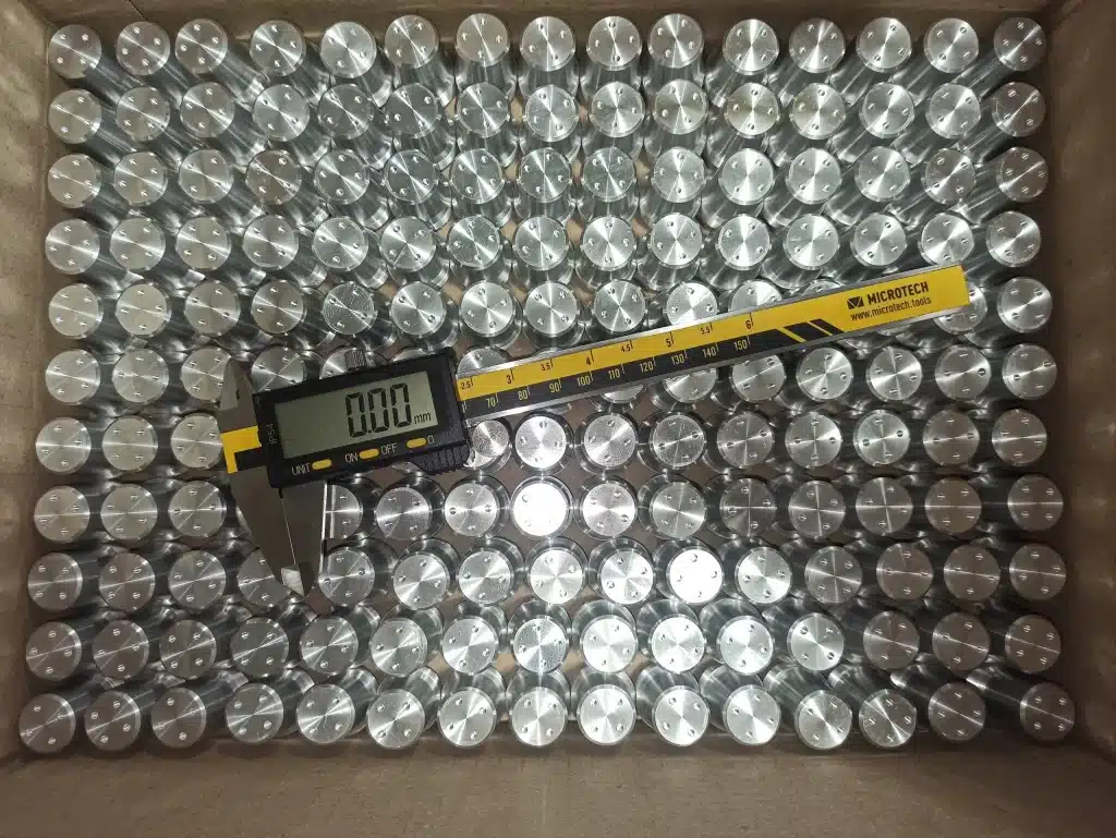 Kiste mit CNC-gedrehten Metallteilen und digitaler Schieblehre zur Maßkontrolle.