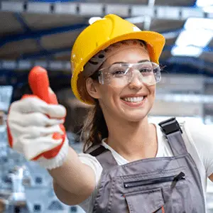 Mitarbeiterin in Schutzkleidung zeigt Daumen hoch in einer modernen Produktionshalle.