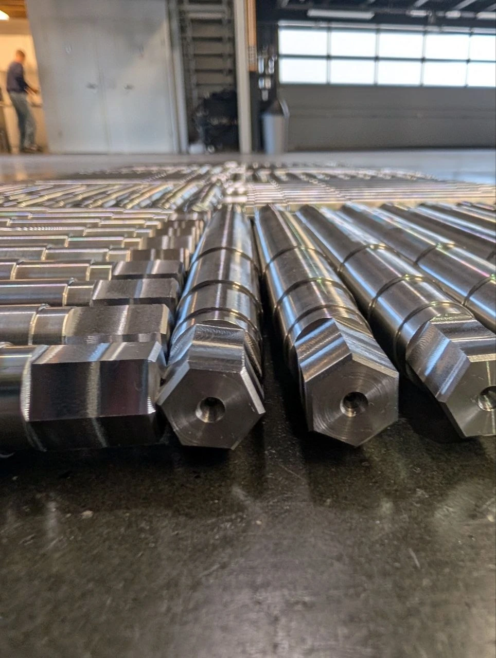 Präzisionsgefertigte Metallwellen mit Sechskantenden und Bohrungen in einer Produktionshalle.